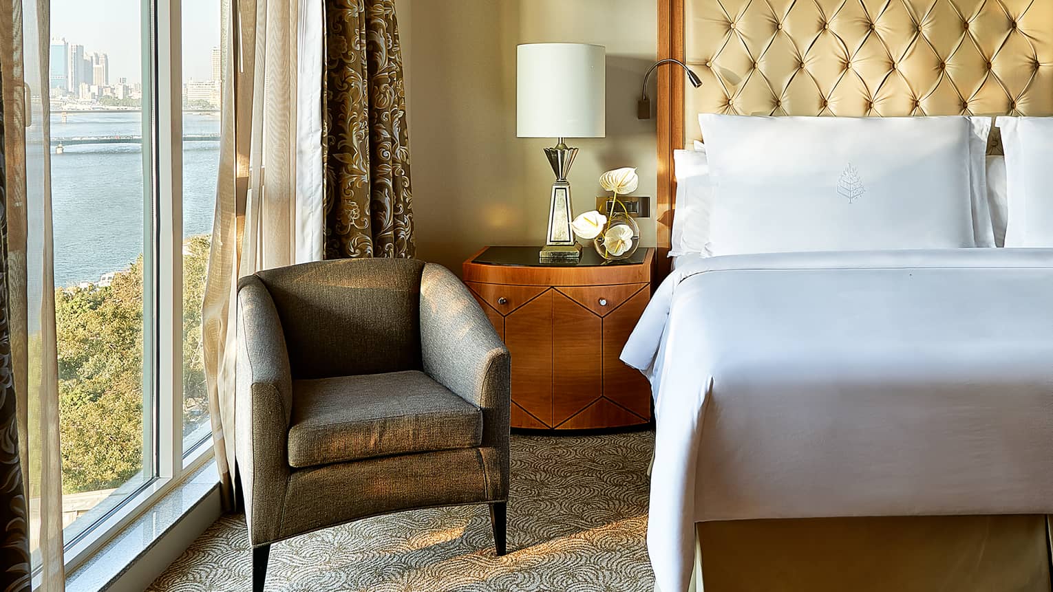 Royal Suite close-up of white pillows and tall leather headboard, wooden side table with lamp and white orchids