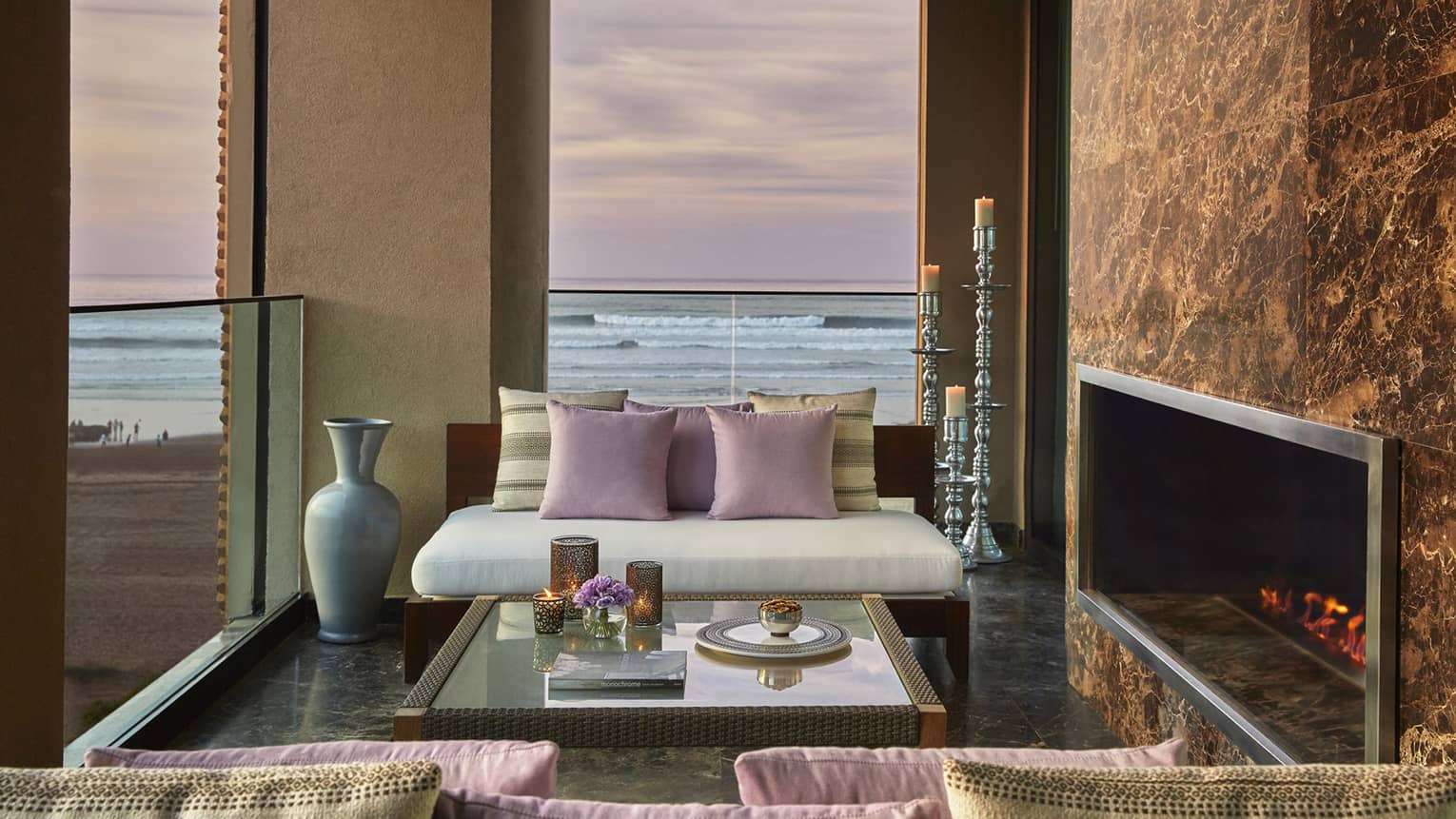 Royal Suite Ocean View white sofa, pink pillows by fireplace, under window with pink sunset, ocean