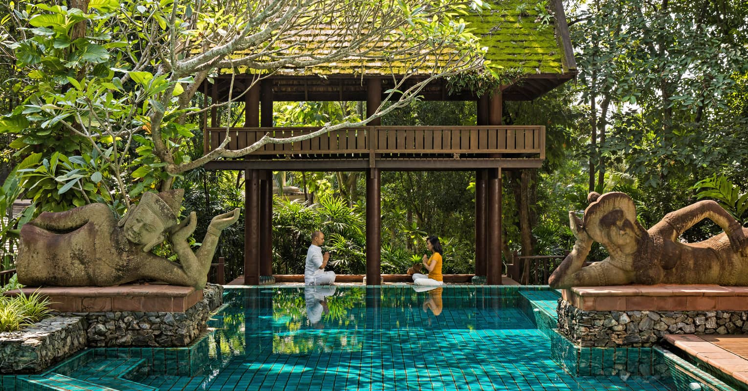 Couple practicing meditation in an outdoor pool setting 