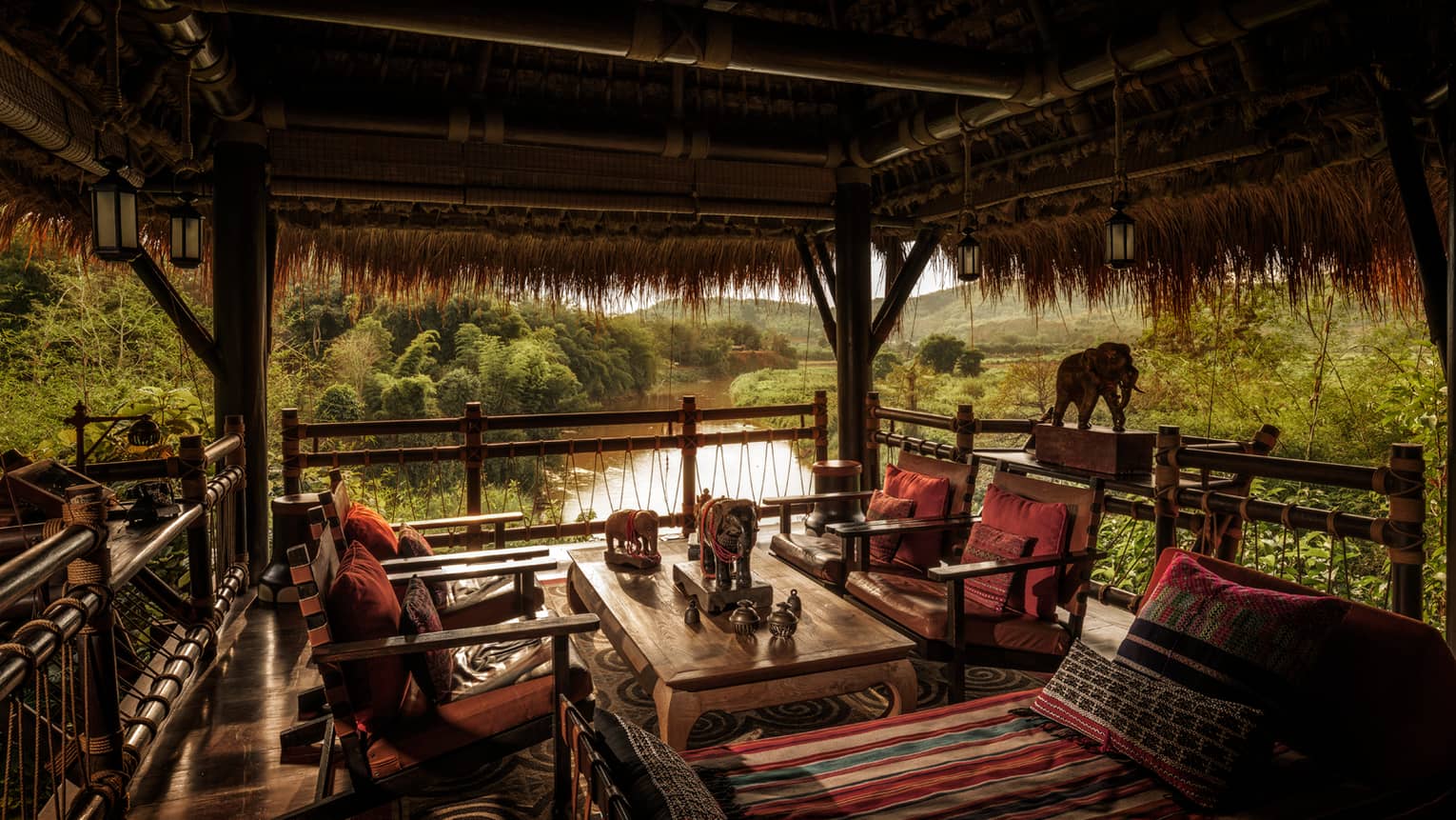 Burma Bar wood tables, chairs with red cushions under thatched-roof cabana