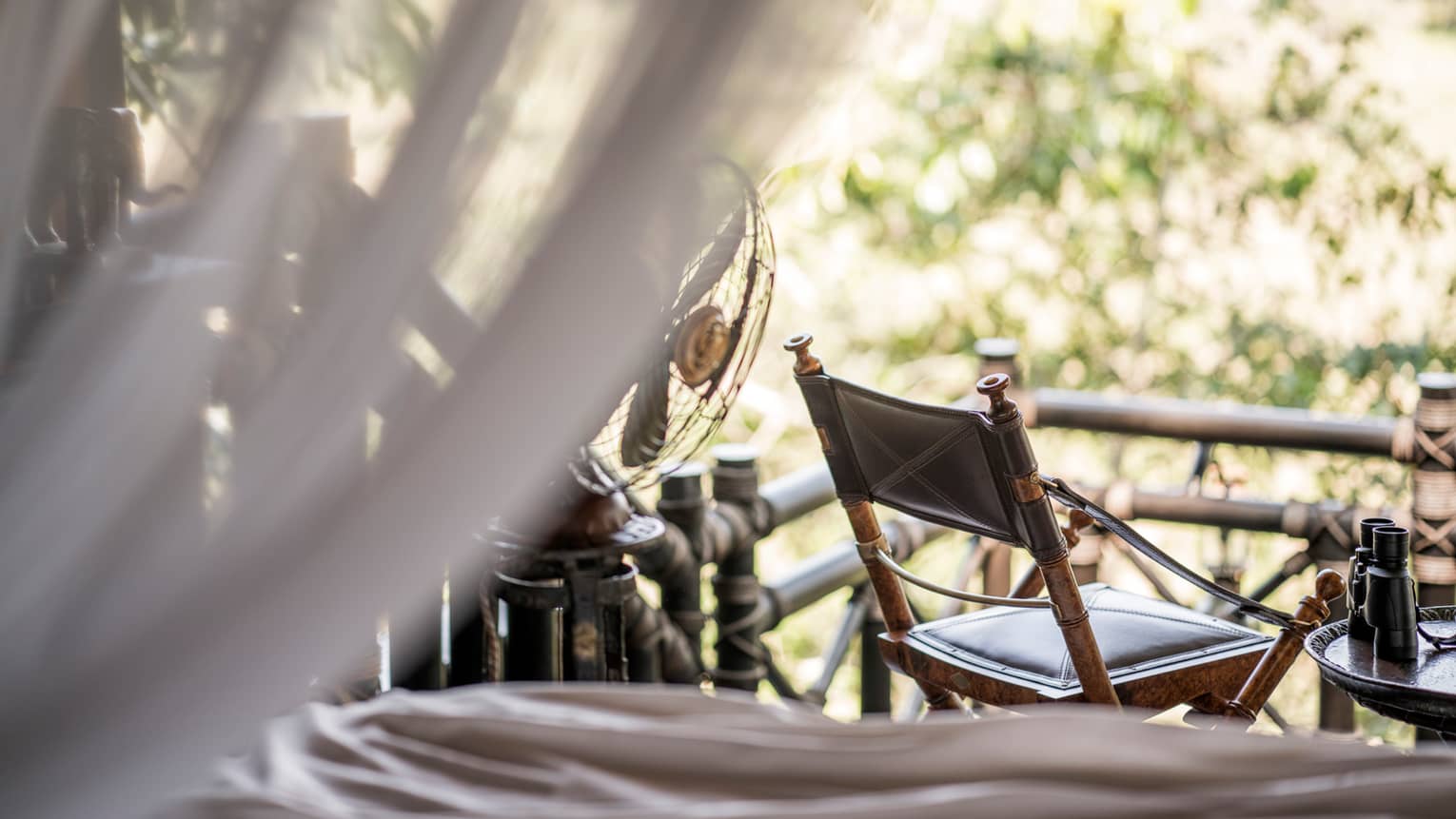 Wood chair at window, view from sheer white net on bed 