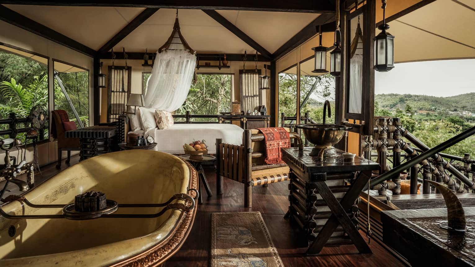 Outdoor open-air room with bed, tub, lanterns, mountain views