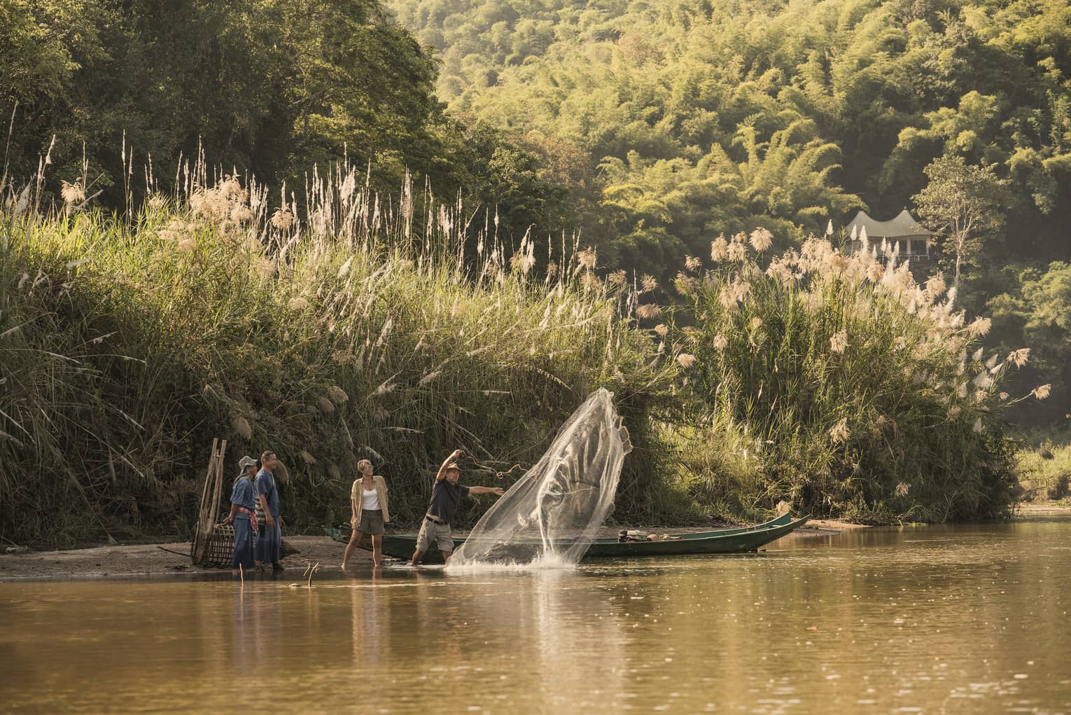 Man throws traditional Thai fishing net from boat into river during group activity