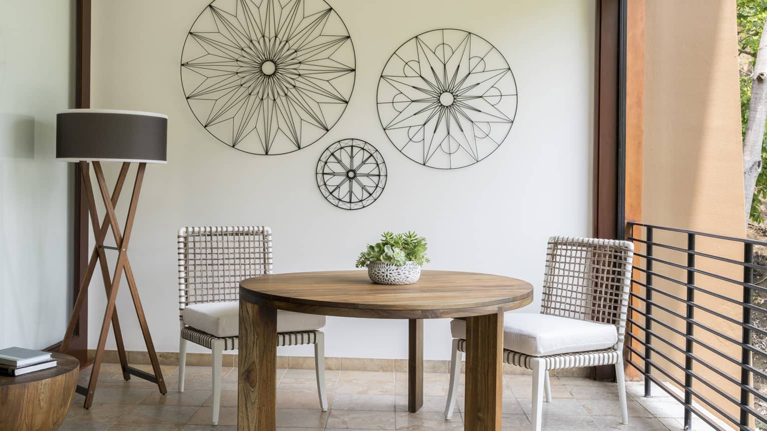 Brisa Room round table with two white wicker chairs on tile terrace, iron decorations on wall