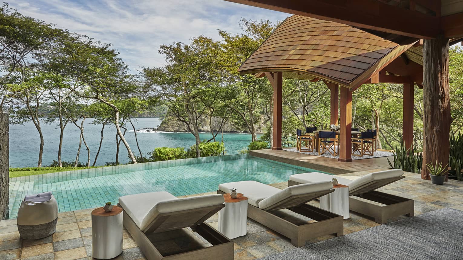 Miramar Suite patio tile patio, three long lounge chairs in front of plunge pool, row of trees, overlooking ocean