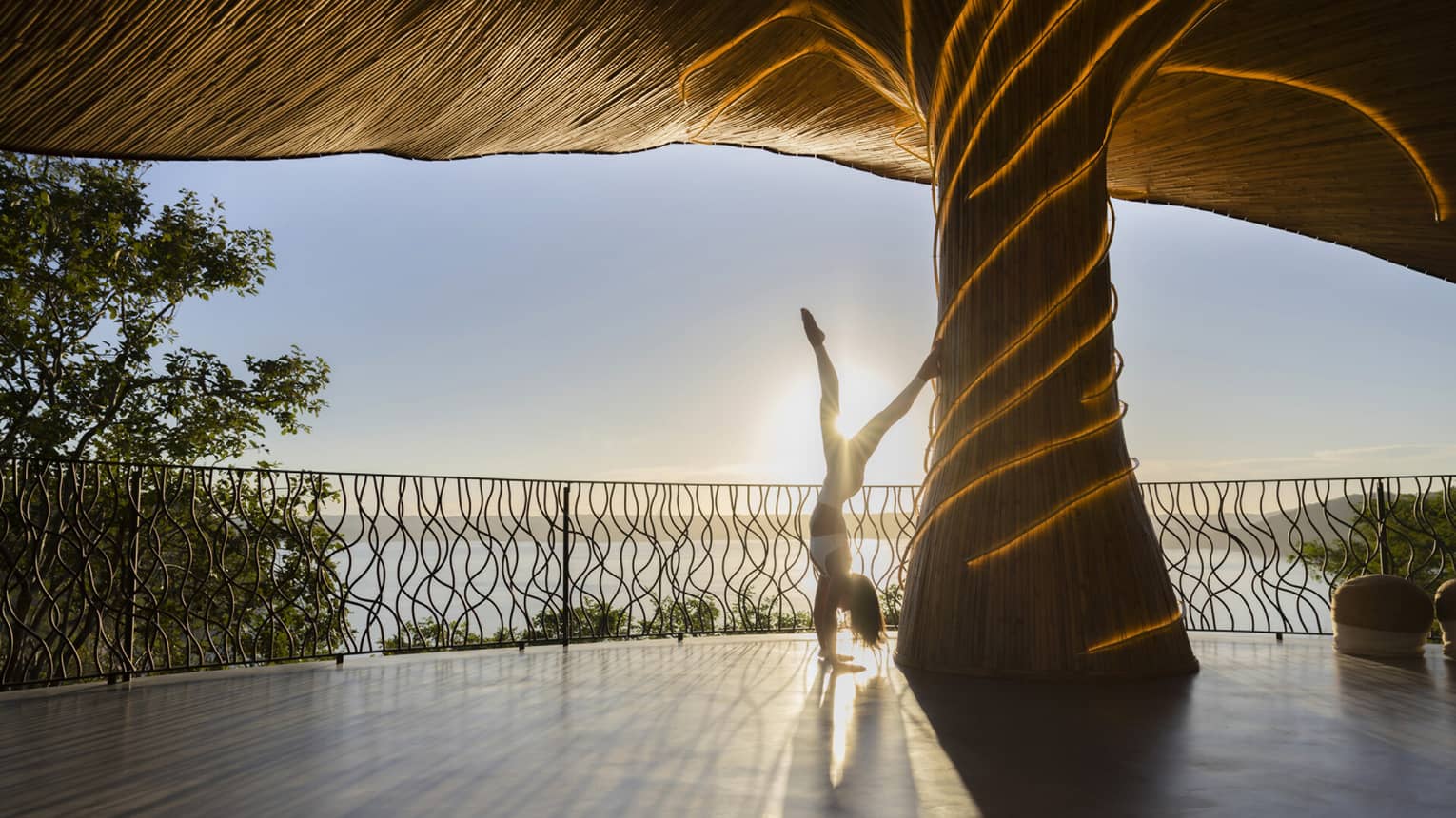 silhouetted person doing a hand stand against a column beneath the Wellness Shala roof as the sun shines in