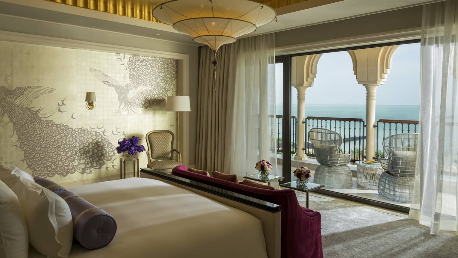 Bedroom suite with decorative wallpaper, red velvet bench, patio with white pillars, wicker chairs