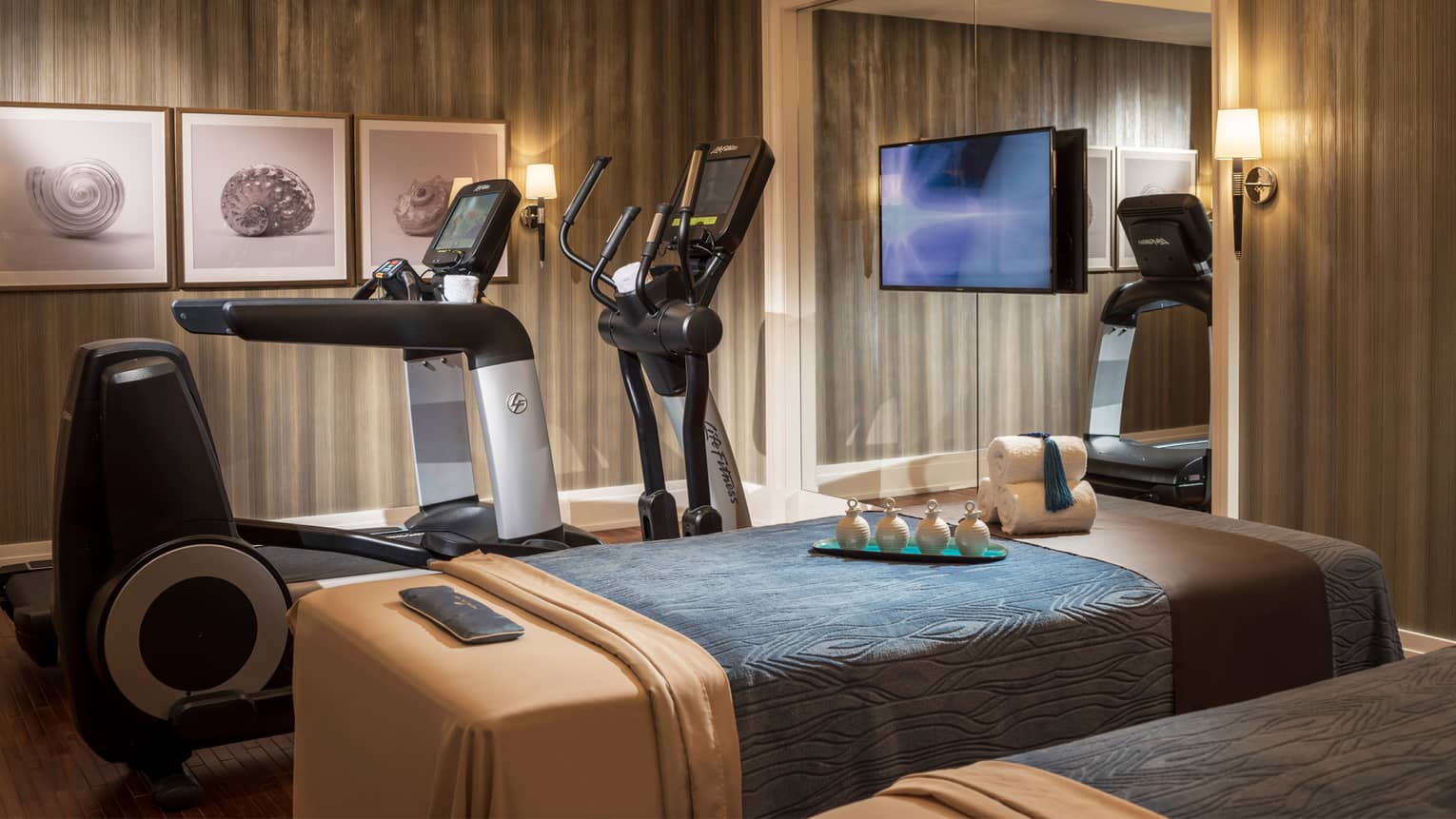 Private room with two massage tables beside two cardio machines, in front of mirror