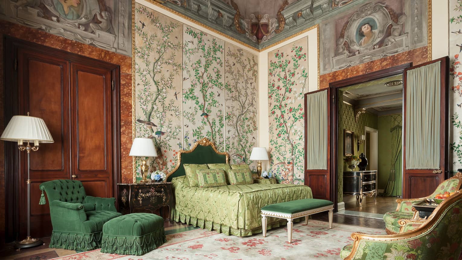 Hotel room with bed, green velvet chair and bench, antique garden wallpaper