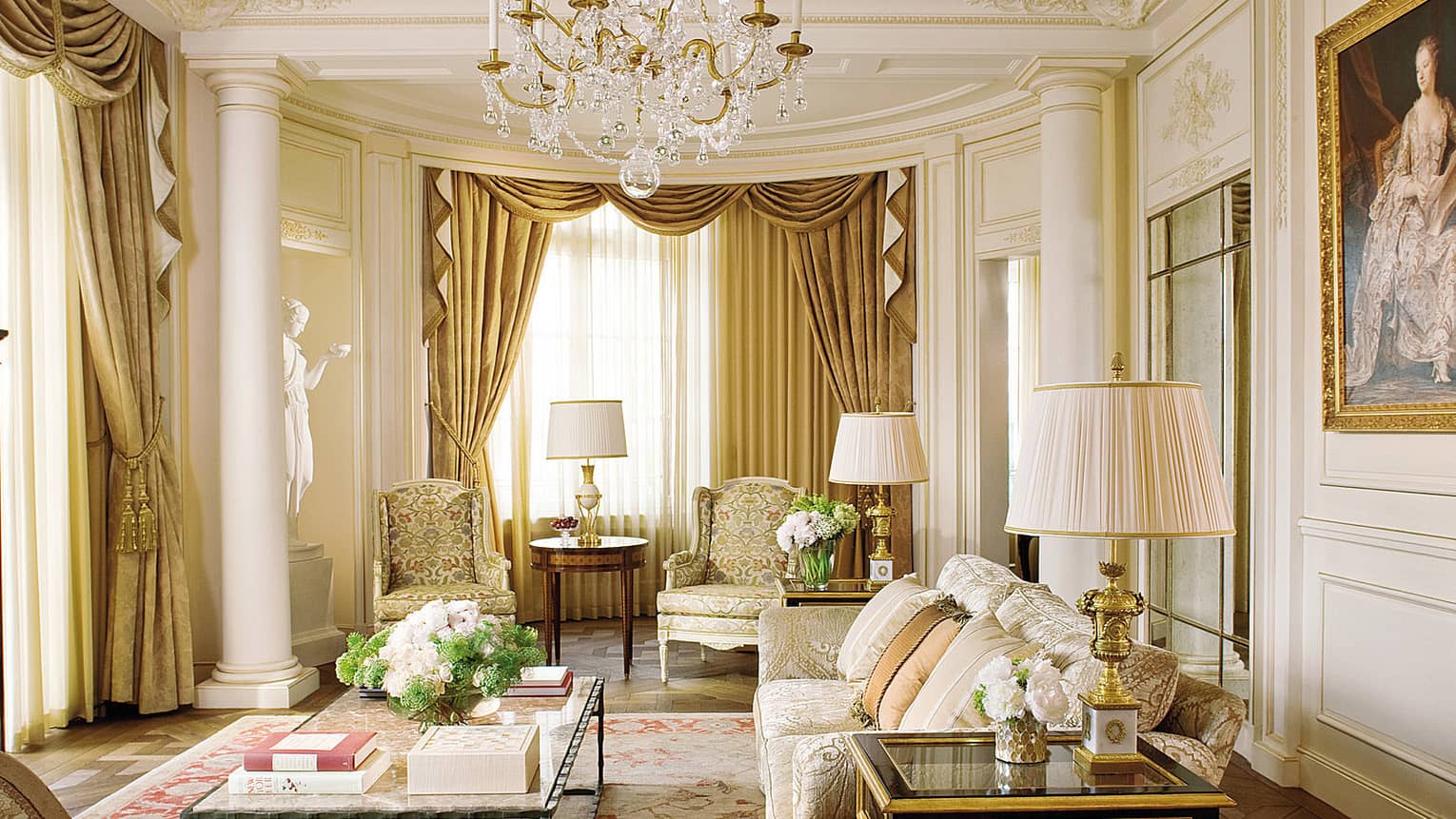 Elegant Royal Suite living room with cream floral sofas and decor, crystal chandelier, white statue, large oil painting