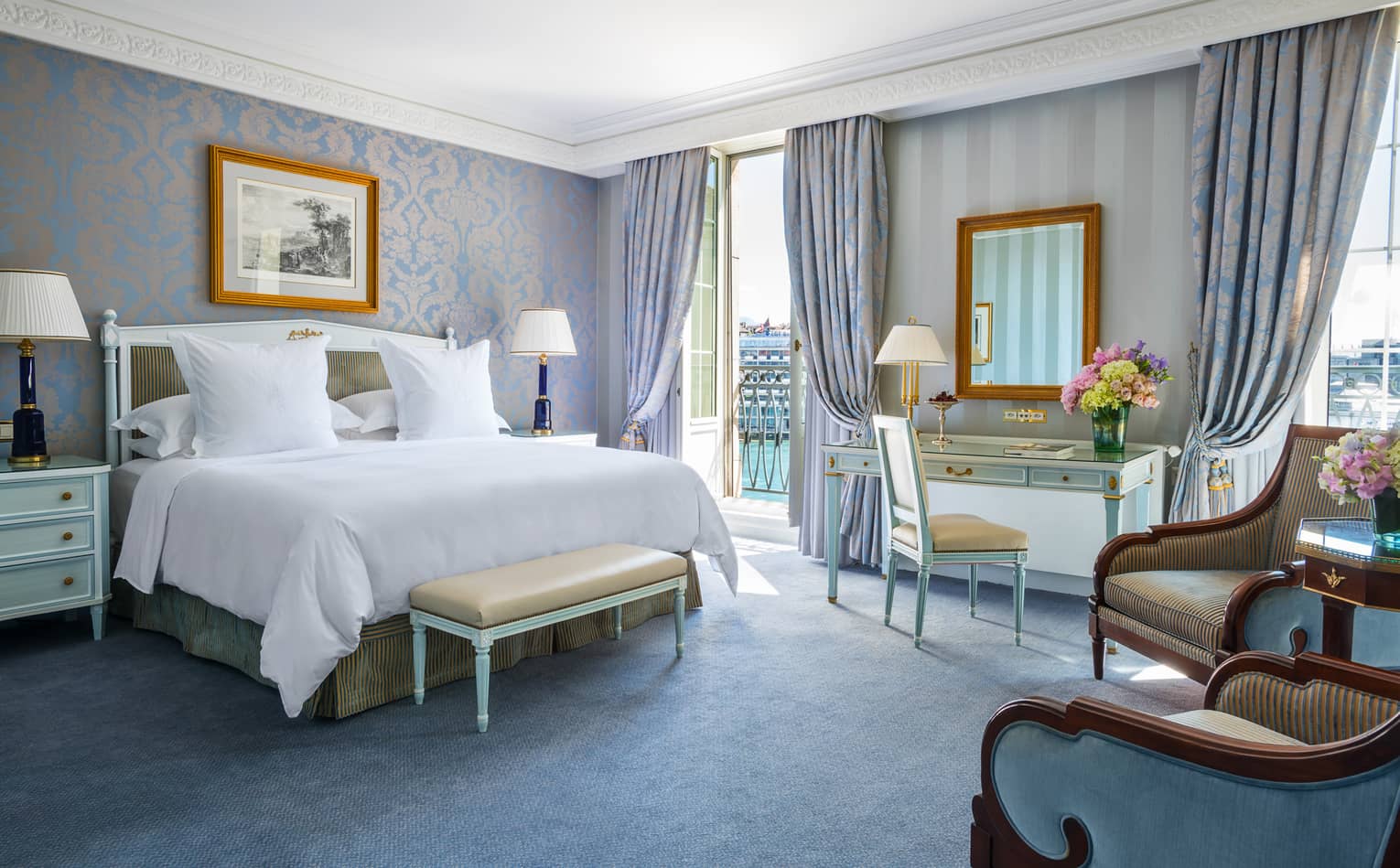 Deluxe Room bed with elegant blue-and-gold wallpaper and decor, floor-to-ceiling French doors opening to patio