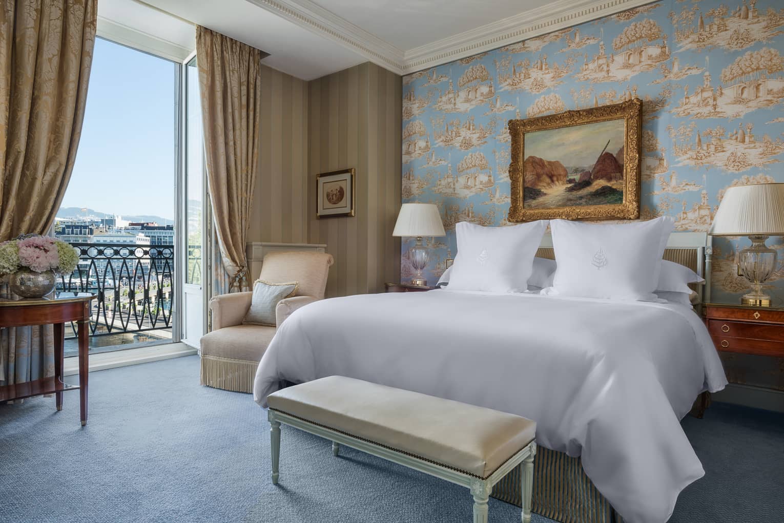 Suite Léman with antique-style blue wallpaper, painting with gold frame above bed next to open French doors with lake view