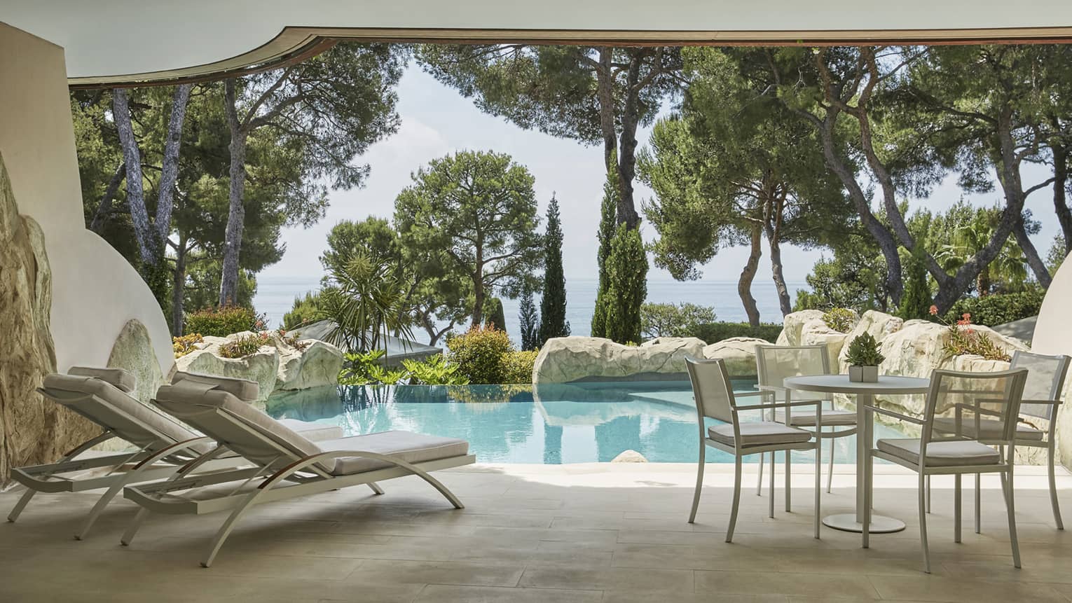 Private stone pool and terrace with two lounge chairs, table and chairs, sea view through greenery