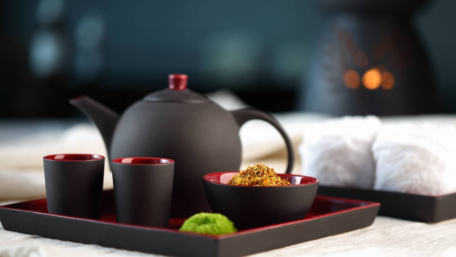 Black-and-red modern teapot with two mugs and bowl of loose-leaf chamomile on serving tray