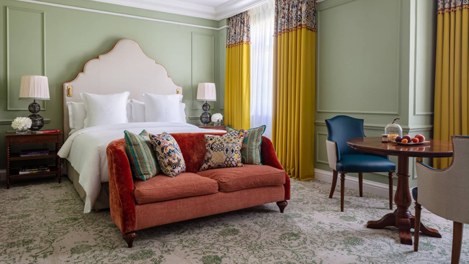 Garden Room with King bed with white linens, red loveseat at foot of bed, table for two, cherry nightstands, floor-to-ceiling window with yellow drapes