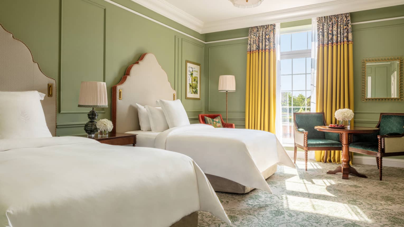 Mews Room with two queen beds, paisley carpeting, avocado-coloured walls, accent table with two chairs, floor-to-ceiling window with yellow drapes