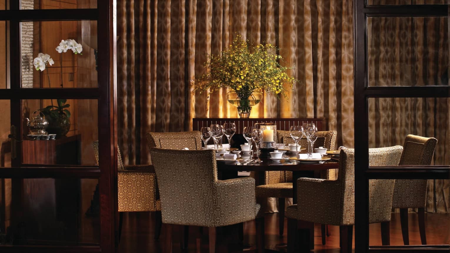 Upholstered dining chairs around wood table in dimly-lit dining area by wall, curtains