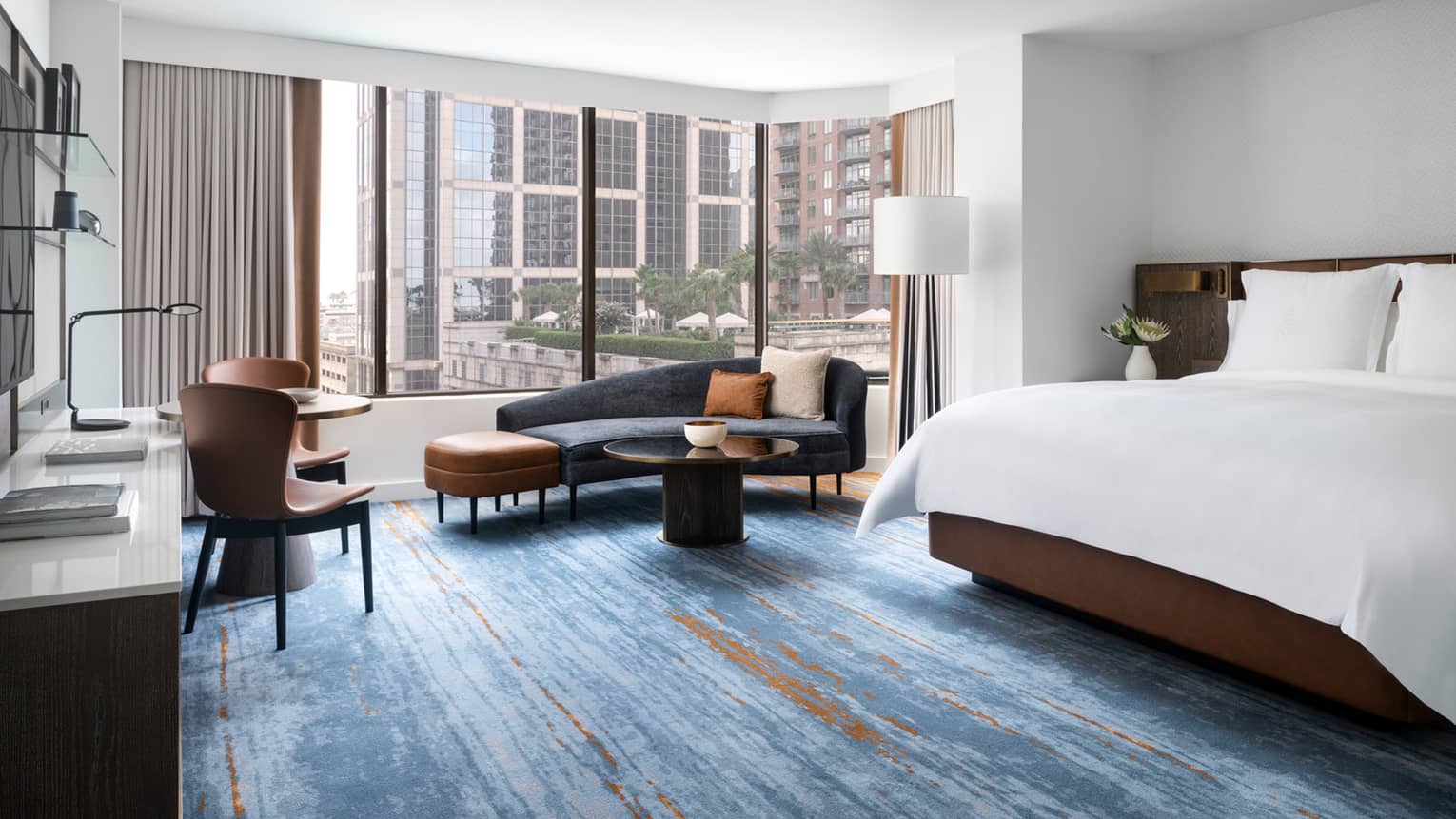 Hotel room with blue carpeting, king bed, dark blue chaise lounge, large windows