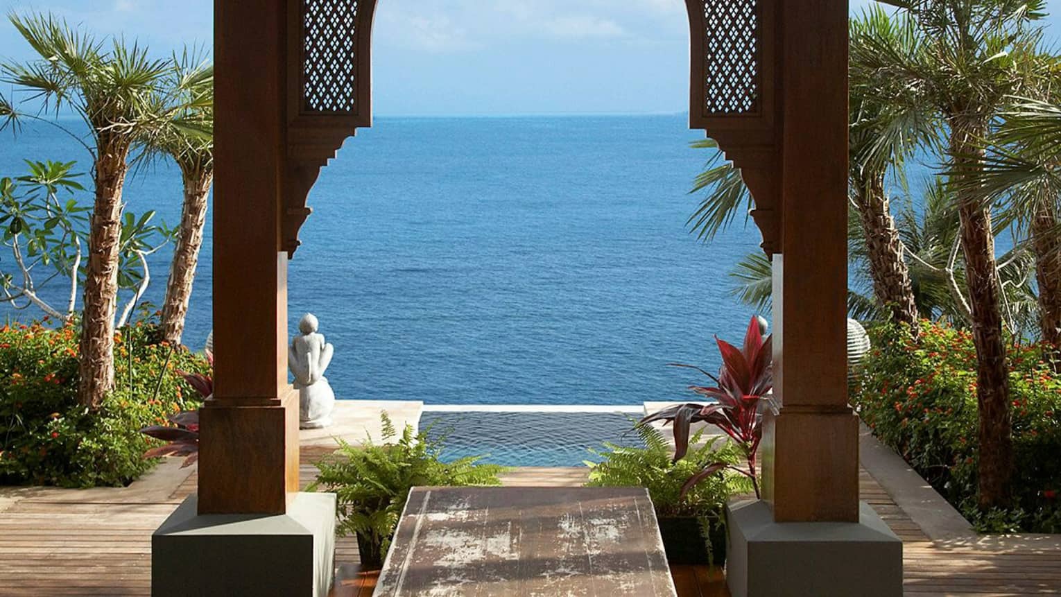 Wood archway, pool palms and ocean under blue sky