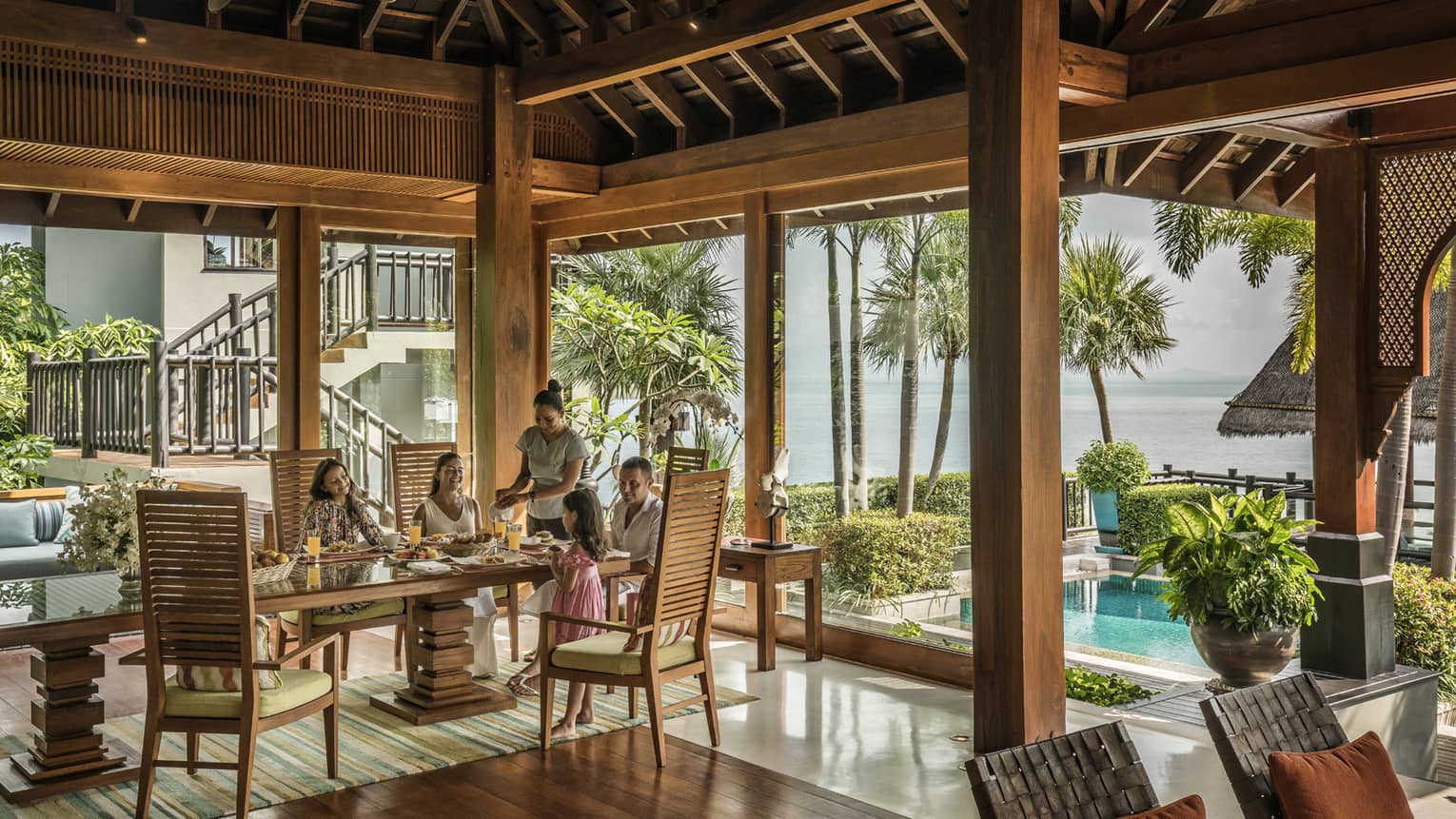 Butler serves family at long table in bright corner window dining room with windows