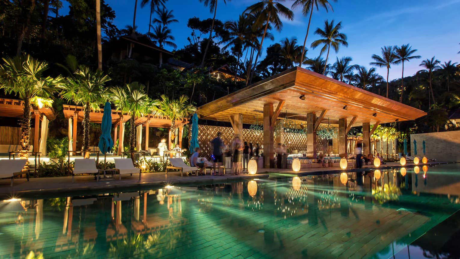 People mingle at CocoRum Bar at dusk, mirror-like pool in foreground 