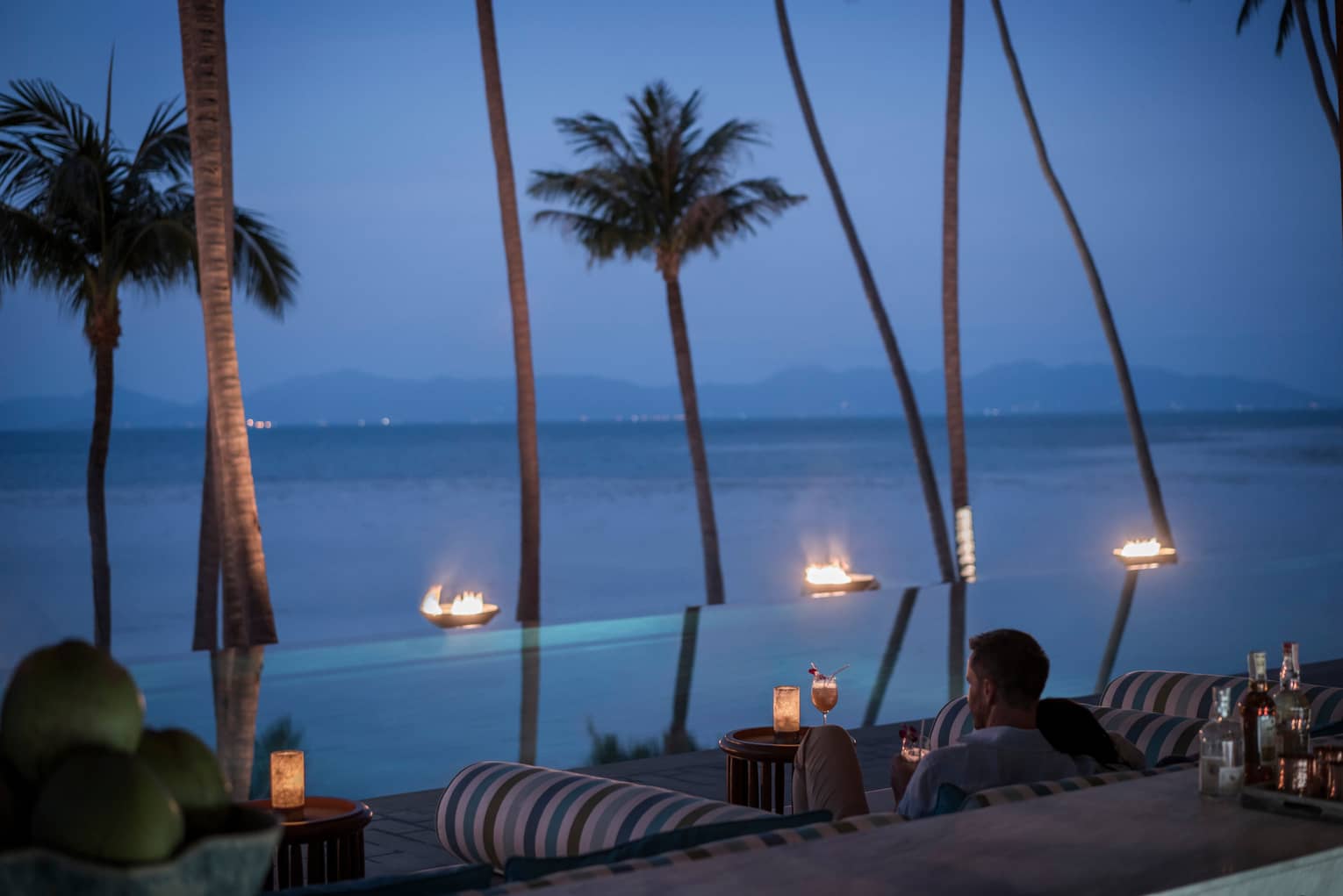 Guests sit outside CoCoRum enjoying drinks by the infinity pool with views of the Gulf of Thailand