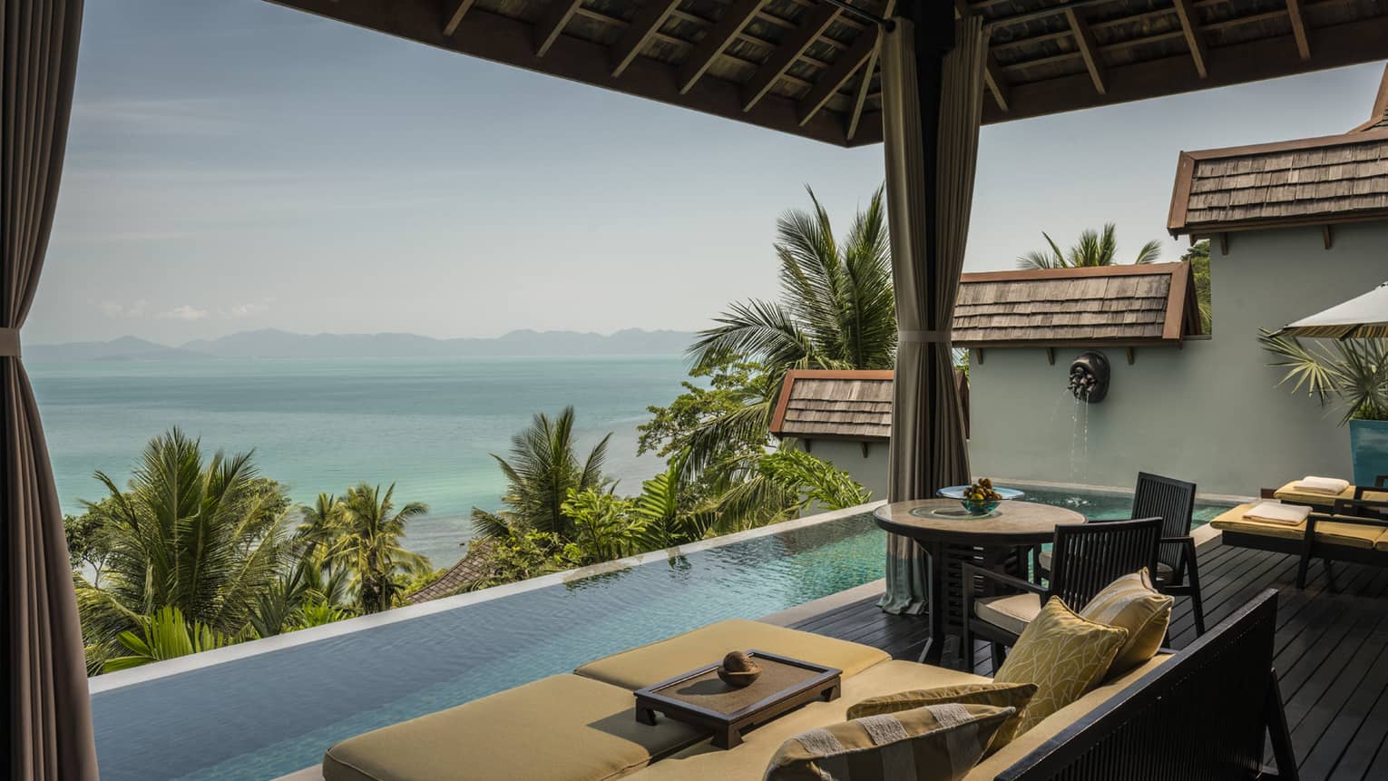 Patio chairs, cushions by infinity swimming pool on villa deck