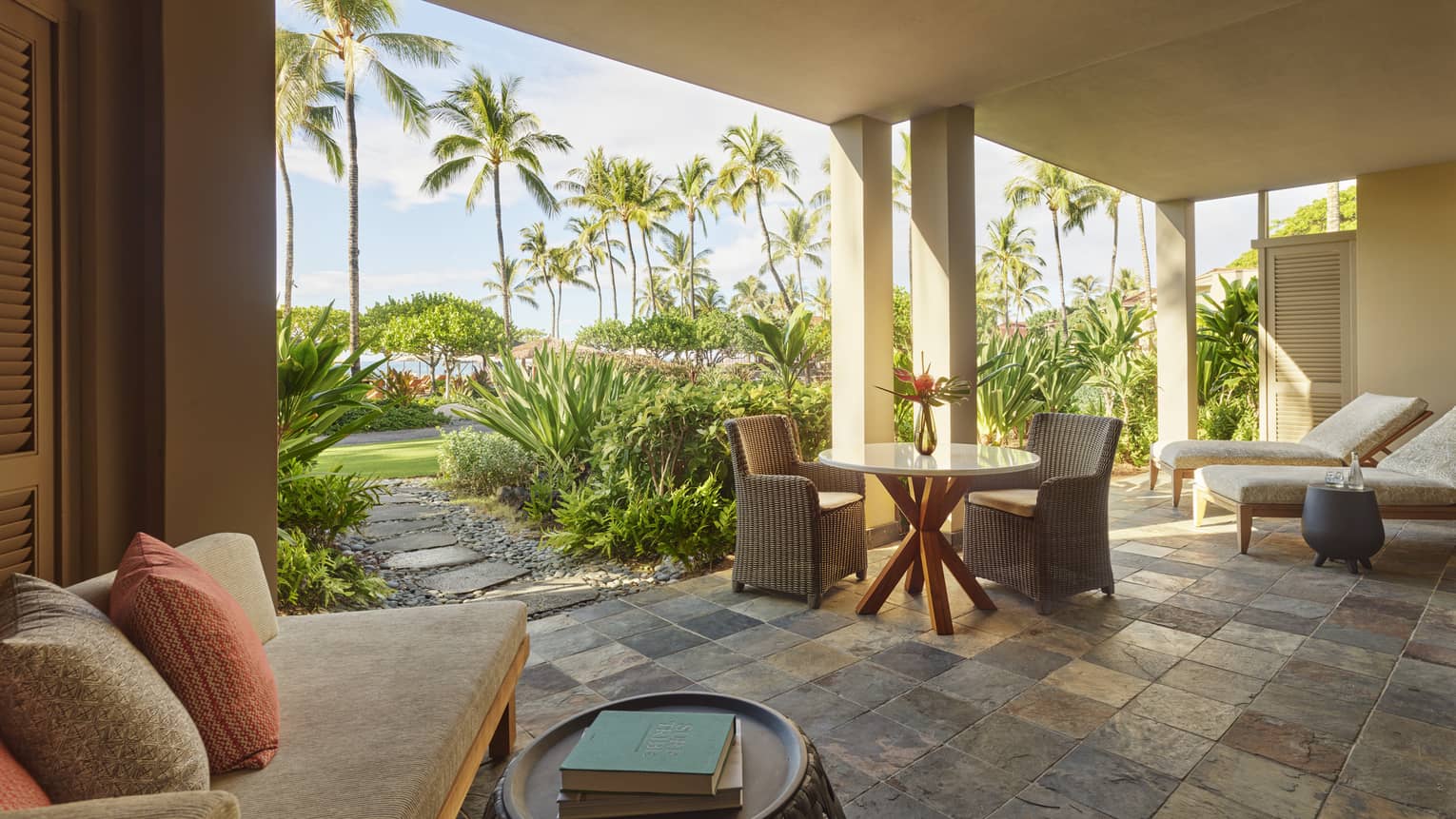 'Ohana Suite covered patio with tiled floor, round table with rattan chairs, tan sofa, white lounge chairs