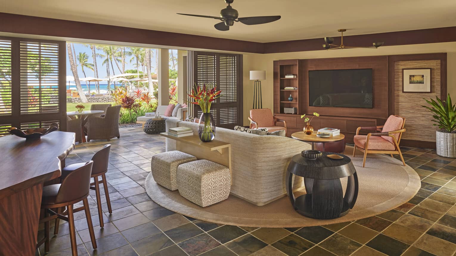 Wai'olu Suite living area with cream sofa, twin coral-coloured arm chairs, wood dining table, doorway to veranda