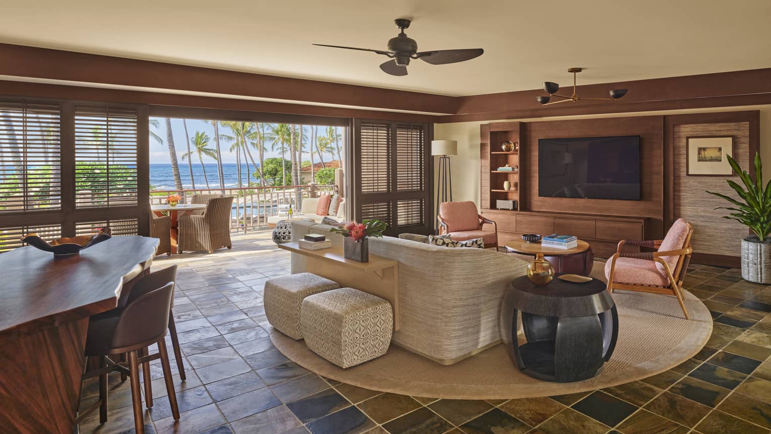 Milo Suite living area with cream couch, twin coral-coloured arm chairs, wood dining table, round area rug, large doorway opening onto balcony