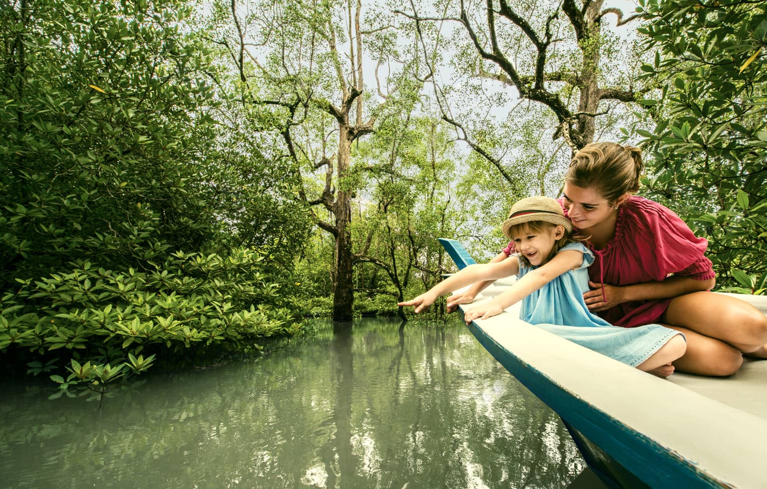 Mom, young daughter in back of wood canoe look into river