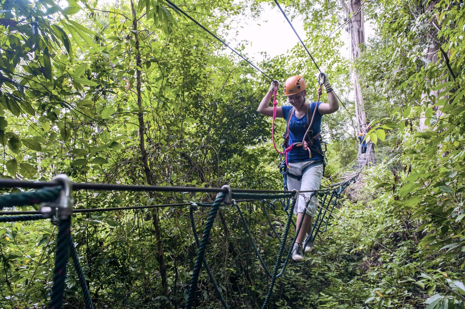 Woman wearing harness walks on ropes above trees