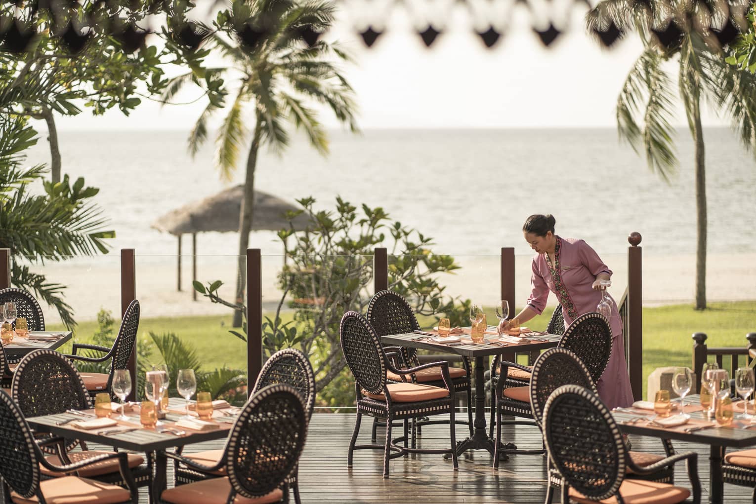 A server at Ikan Ikan sets a table on the outdoor terrace overlooking the beach