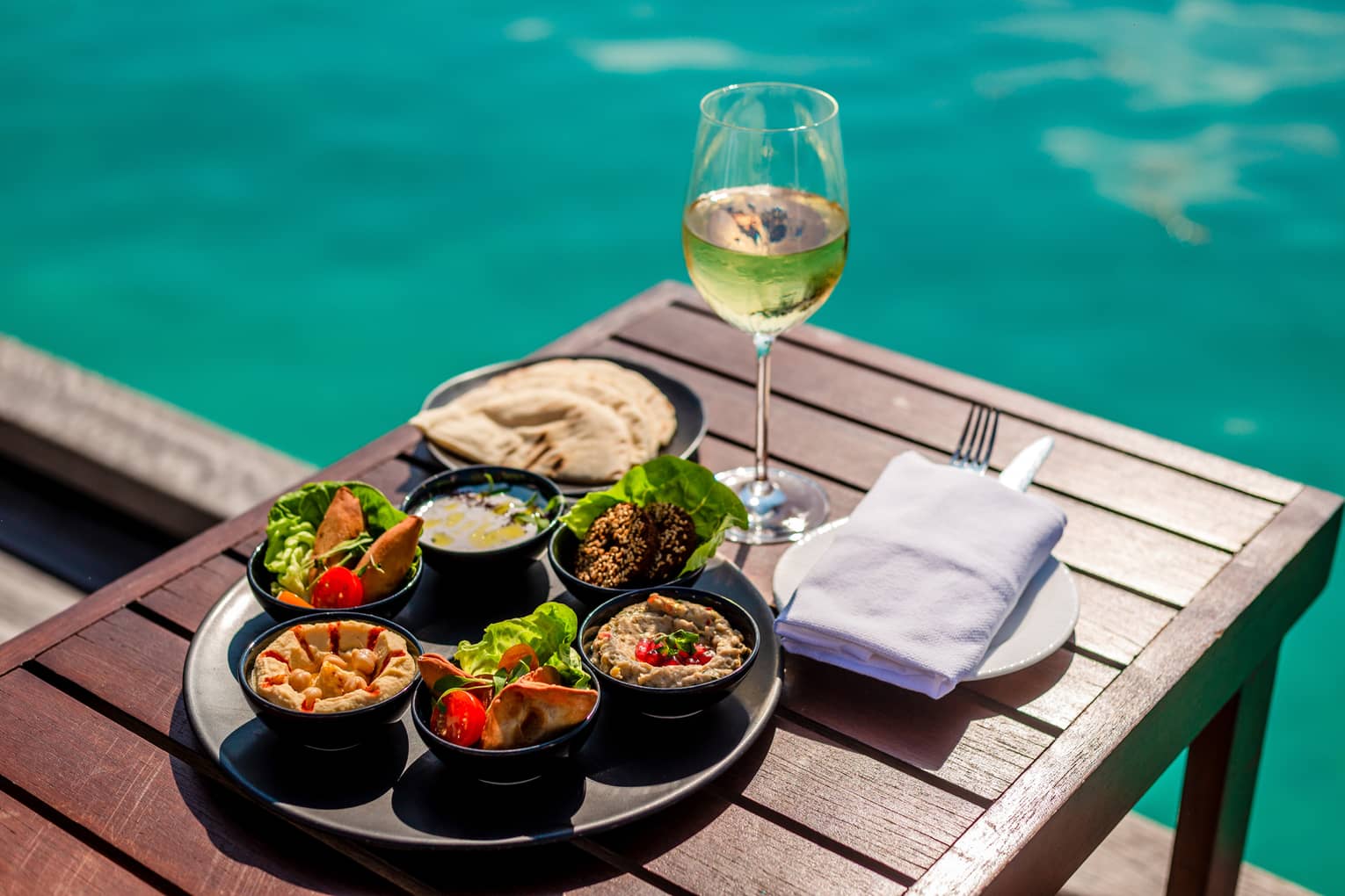 Arabic mezze platter and glass of white wine on poolside table