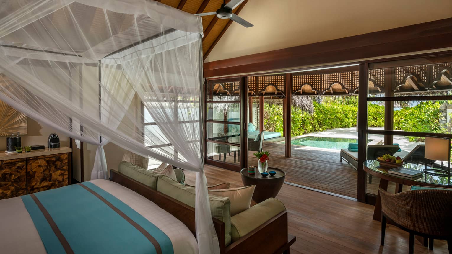 Beach bungalow canopy bed and sofa in front of open-air wall leading to deck and private plunge pool