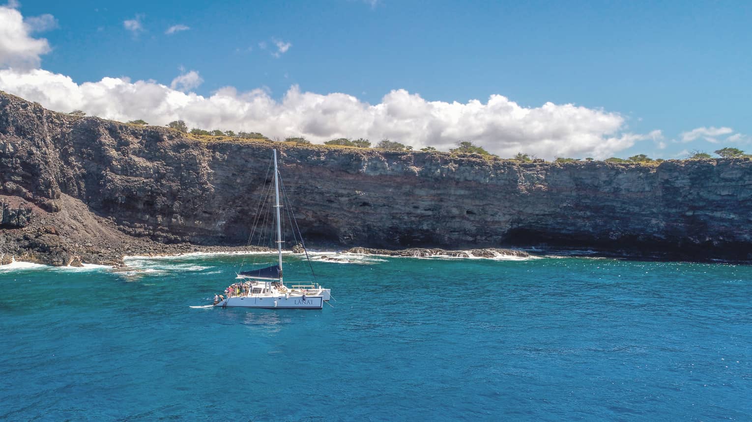 Group of people at end of white catamaran boat on ocean near rocky cliffs