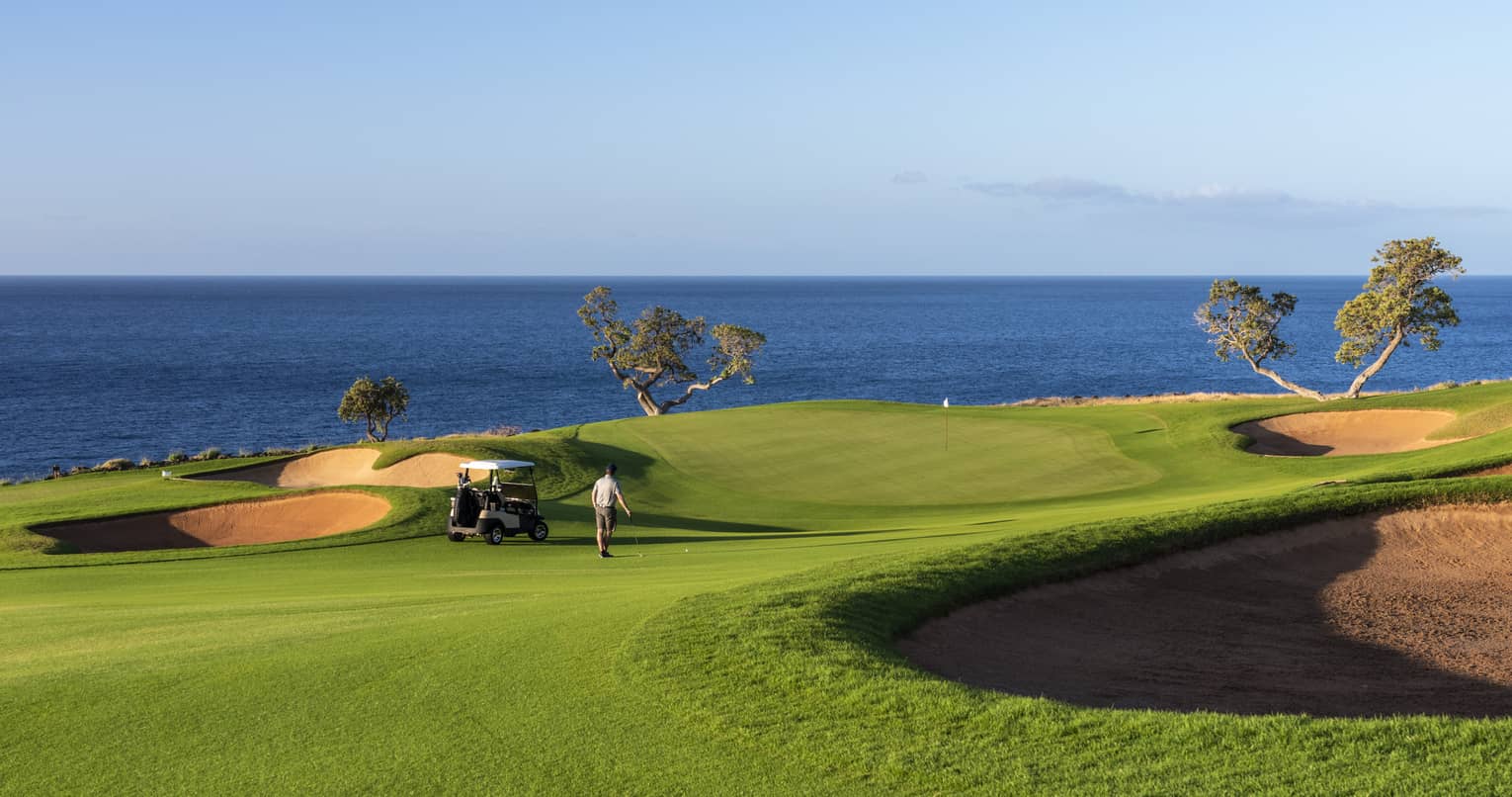 Golfers walk across sweeping green lawn on golf course beside ocean