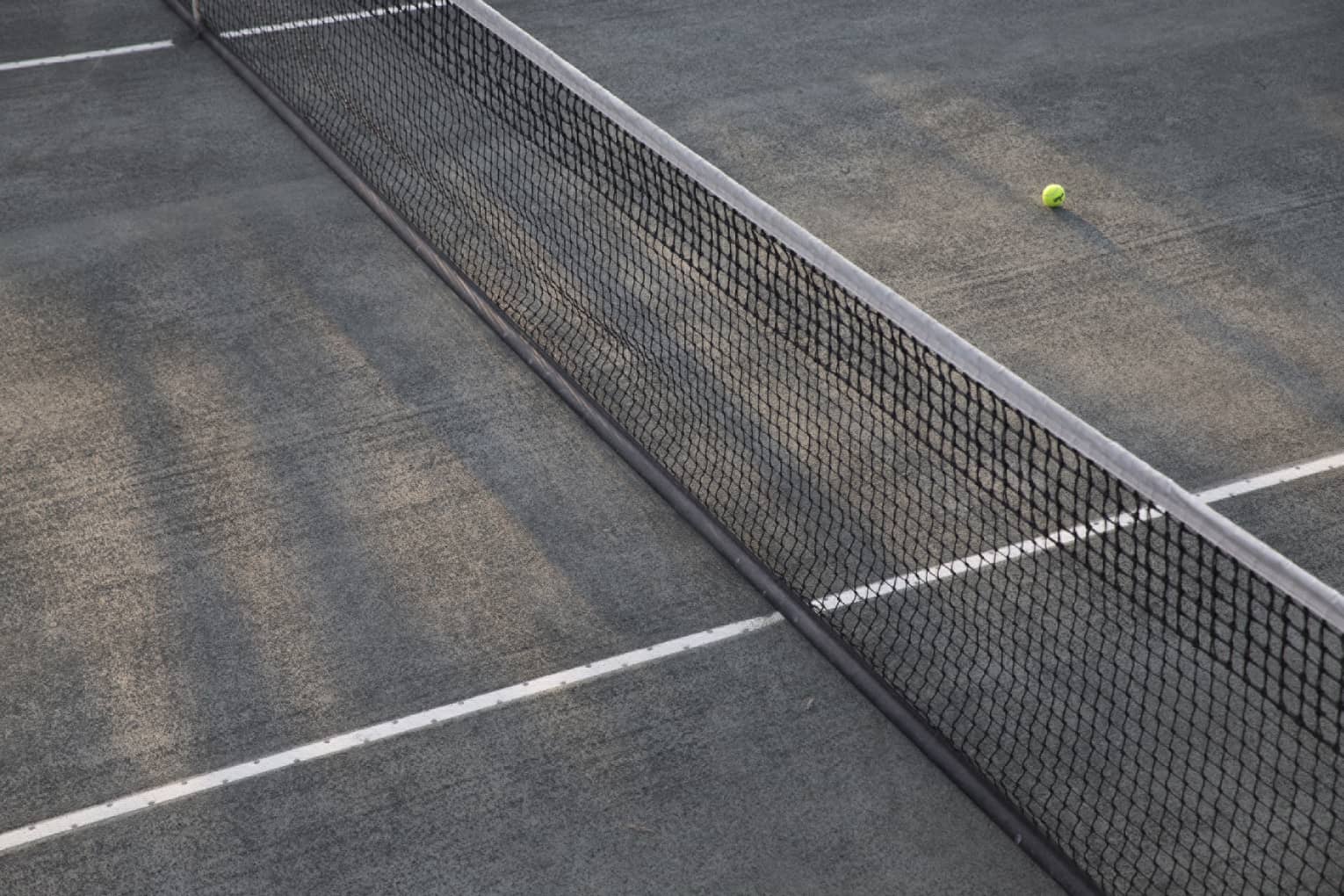 A lone tennis ball lies near the net on an empty court