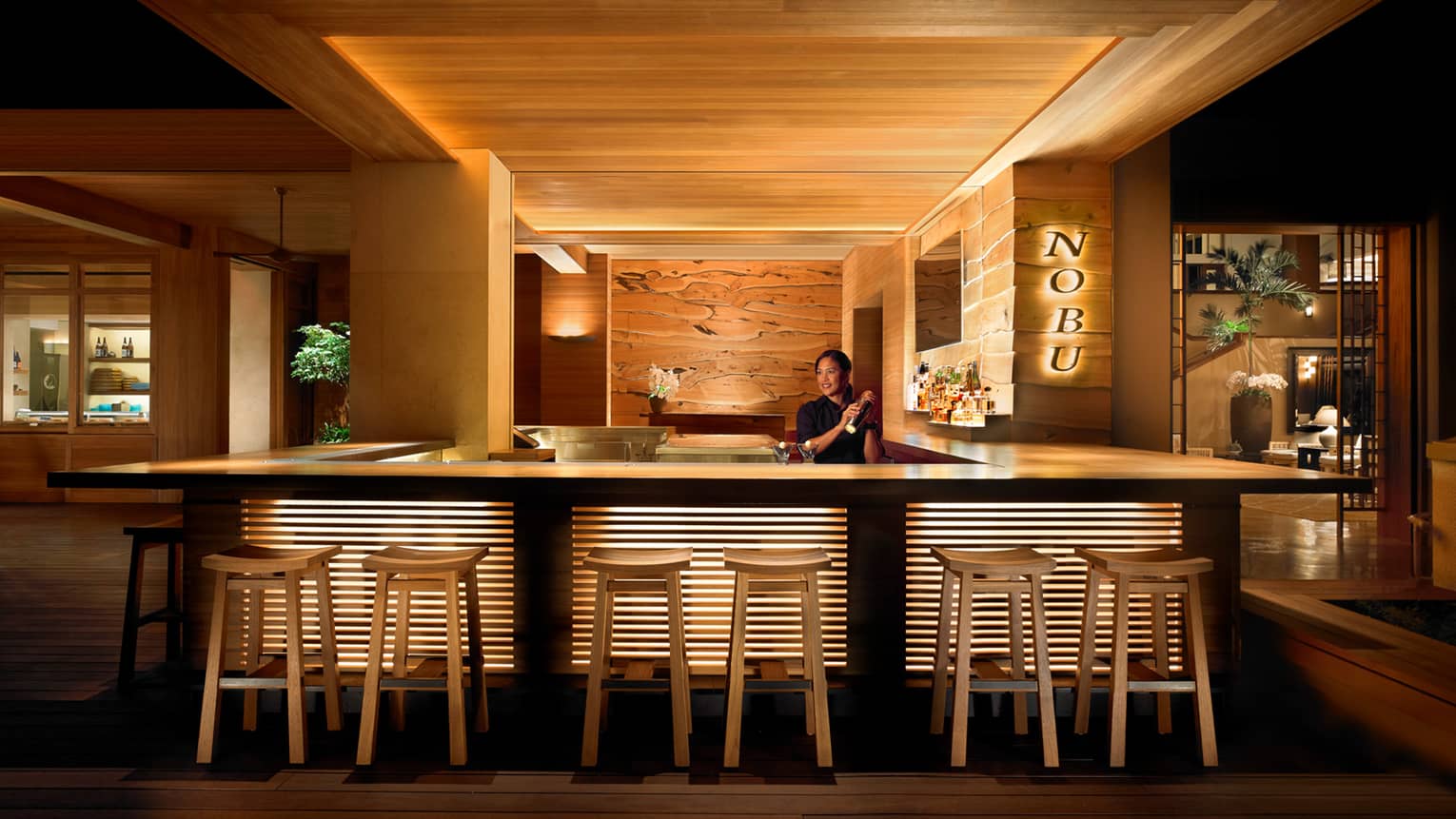 Bartender shaking cocktail behind stool-lined bar at NOBU restaurant