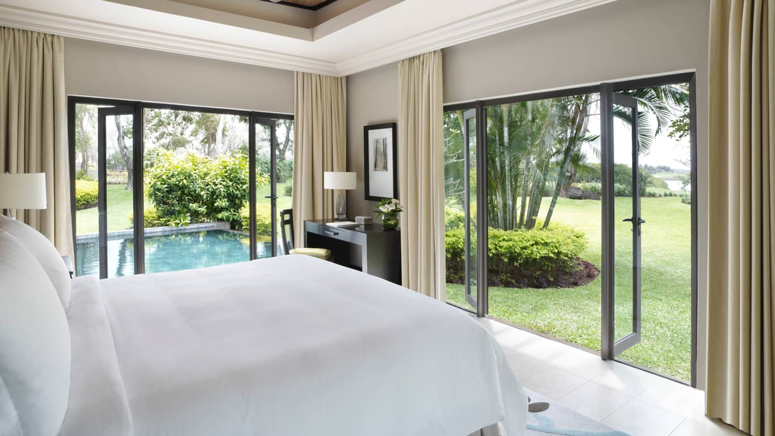 Deluxe Residence Villa side of bed with white linens, open corner patio doors, plunge pool