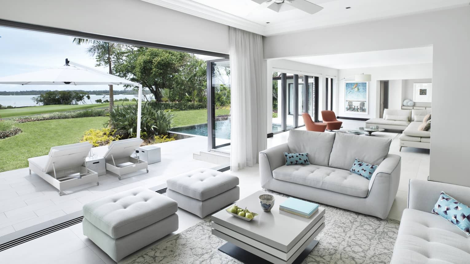 Suite with two white sofas, aqua pillows, two ottomans, square coffee table, patio and water view