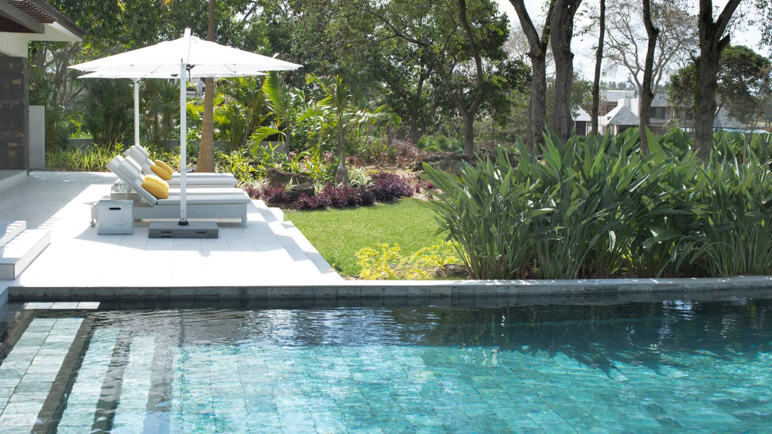 Stone steps leading into villa plunge pool, two white lounge chairs, umbrella on deck