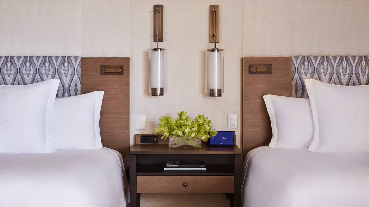 Close-up of two double beds with brown headboards with nightstand and reading lamps in middle