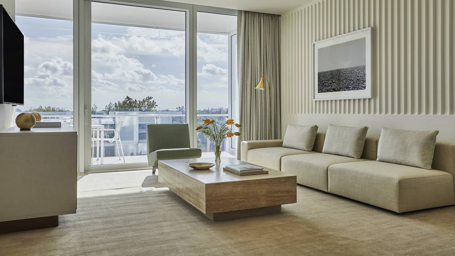 Low beige sofa, wood table in bright seating area by glass balcony doors