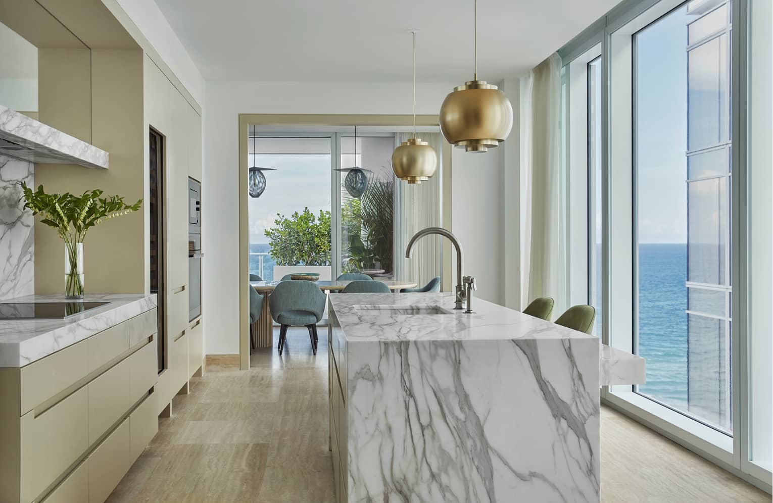 Retro-style brass lamps above grey marble kitchen island, glass wall with ocean views