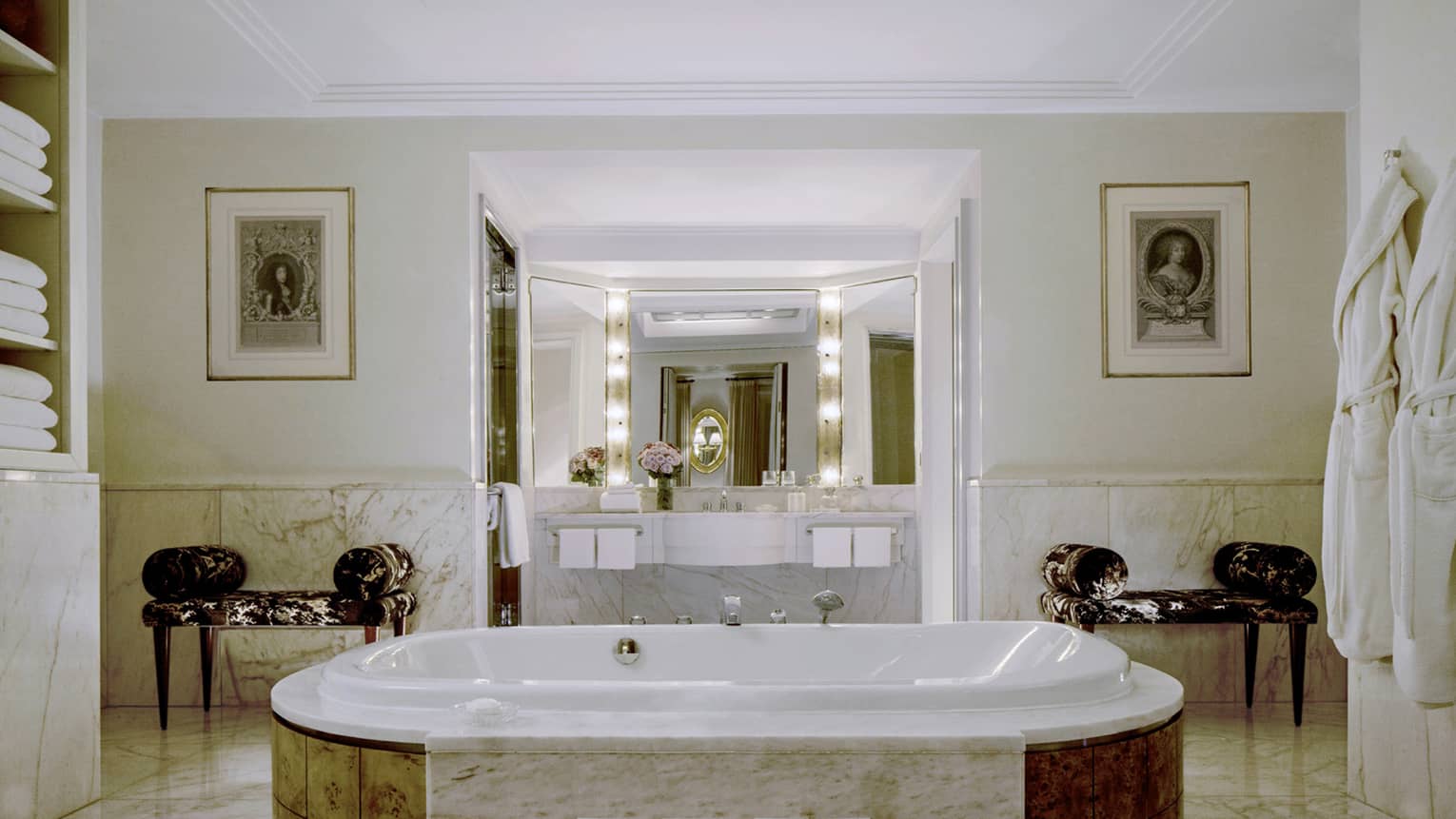 Full marble hotel bathroom with Hollywood lights over vanity, two benches and jetted tub in centre