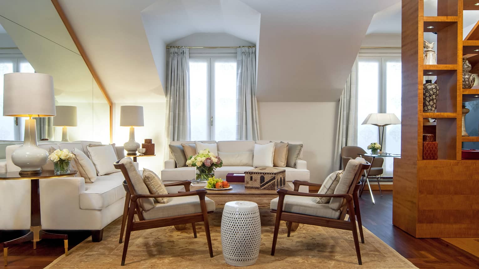 Hotel suite with white sofa seating vignette and two armchairs flanking white garden stool