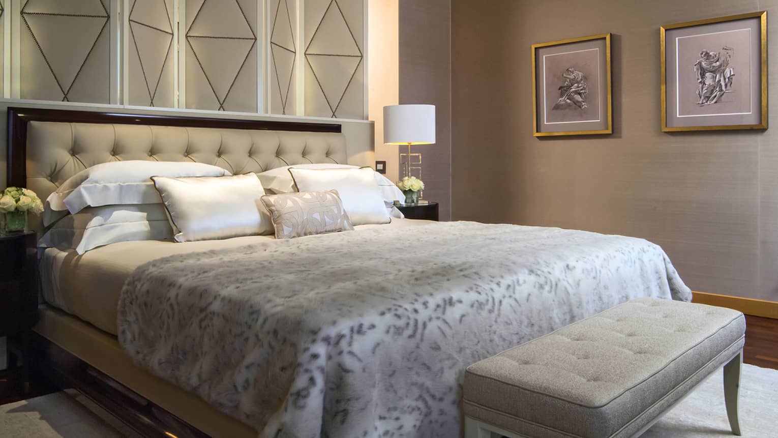 Neutrally dressed hotel bed with tufted headboard with footboard and against geometric wall