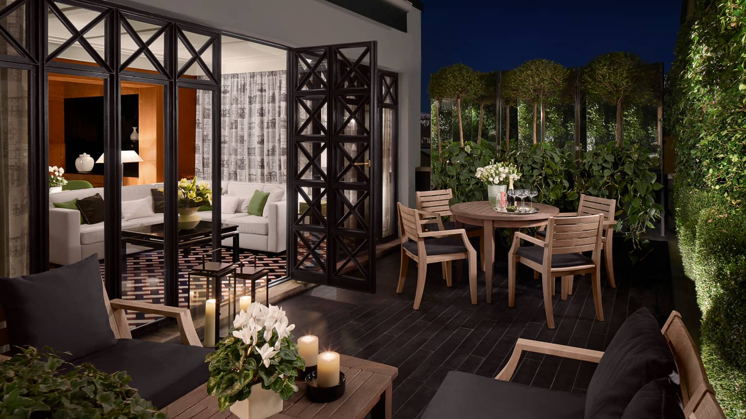 Balcony with wood tables and candles, chairs with black cushions, open doors to suite, white sofa