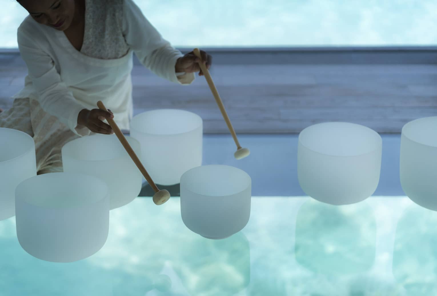 Spa staff plays various white crystal bowls with wood mallets during sound healing session